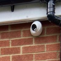 Close up of white security camera underneath black guttering